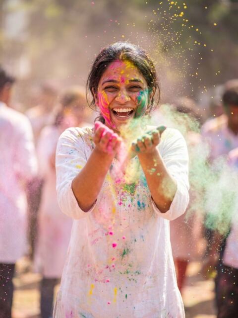 The female sample face in white, holding out palms full of Holi colour